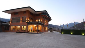 A two-story building with traditional architecture, featuring a large entrance with a covered porch and multiple windows. - Paro Grand Resort (Paro)