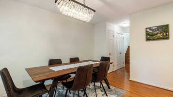 Un coin repas avec une table en bois, six chaises, un lustre, un tapis et un tableau accroché au mur.