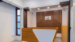 A reception desk with a wooden finish and a white panel, a wooden slat wall with a logo, and a door with a metal handle. - Treebo The Grand Skyla, Malleshwaram (Bengaluru)