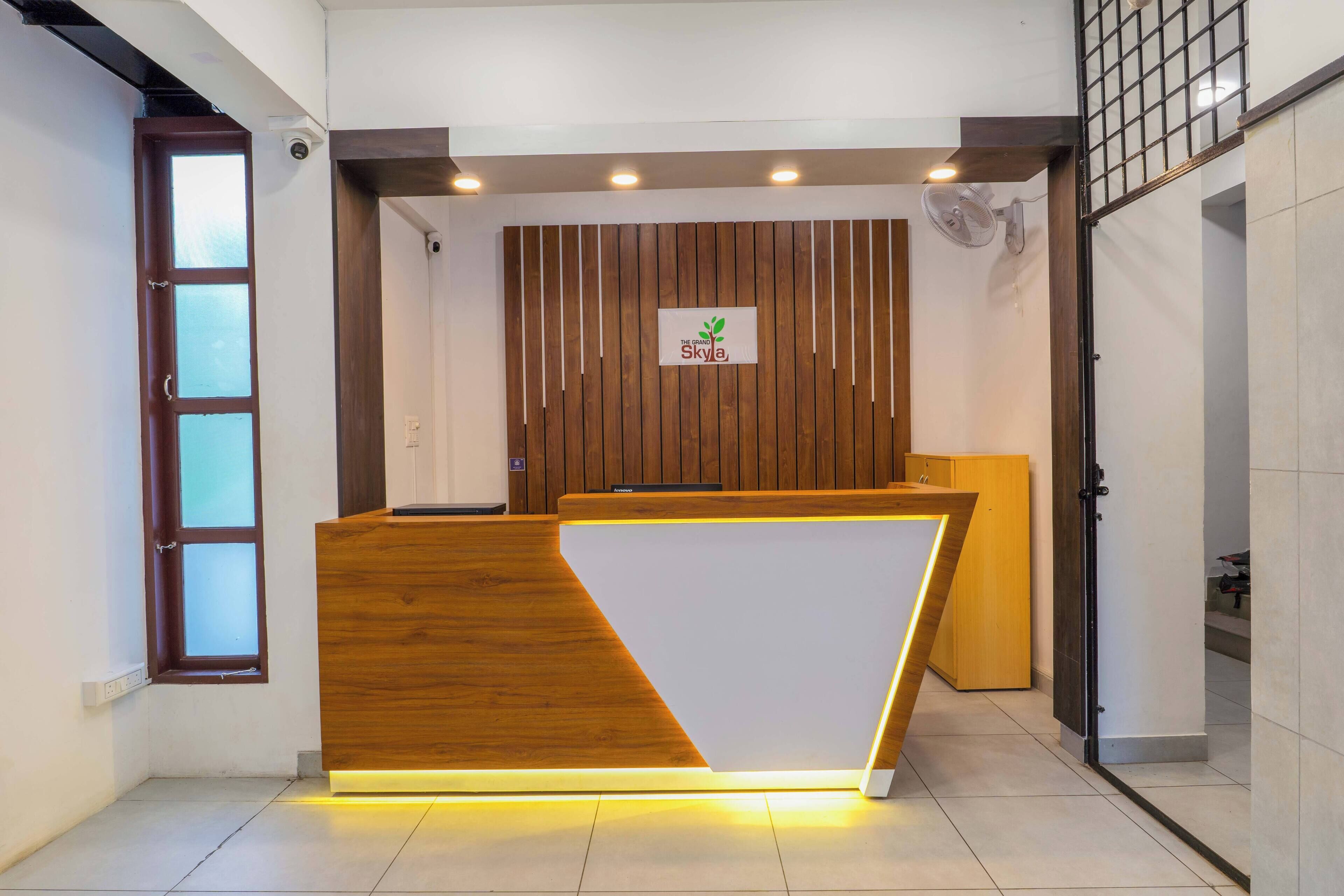 Un mostrador de recepción con acabado de madera y panel frontal blanco, un letrero con un logotipo y una lámpara moderna en el techo.