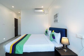 A hotel room with a bed, a nightstand, a lamp, an air conditioning unit, and a painting on the wall. - Treebo The Grand Skyla, Malleshwaram (Bengaluru)