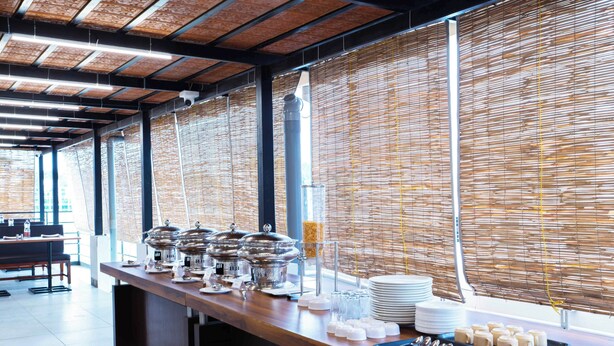 A buffet setup with various food containers and utensils, a glass dispenser, and a stack of plates. - Treebo The Grand Skyla, Malleshwaram (Bengaluru)