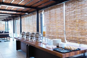 En buffet med forskellige madbeholdere, bestik og et glasdispenser samt en stabel tallerkener.