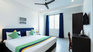 A hotel room with a bed, a ceiling fan, a nightstand, a desk, a chair, a TV, and a window with curtains. - Treebo The Grand Skyla, Malleshwaram (Bengaluru)