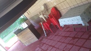 Una habitación con piso de baldosas, una mesa con mantel estampado y varias sillas de plástico.