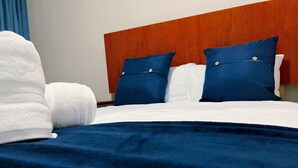 A neatly made bed with white linens, a dark blue blanket, and two matching blue pillows. - Molma Lodge (Greater Tubatse)