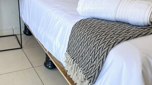 A neatly made bed with white linens, two dark blue pillows, a white towel, and a patterned throw blanket. - Molma Lodge (Greater Tubatse)