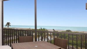 Een balkon met uitzicht op het strand, rieten meubilair en een laptop op de tafel.