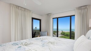 Een slaapkamer met een groot bed, uitzicht op zee en een balkon met een stoel en een lamp.