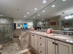 Features a large vanity with dual sinks, glass-enclosed shower, and a large mirror.