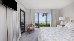 Une chambre d’hôtel avec un grand lit, une chaise, une télévision, une table de chevet et une vue sur la plage.
