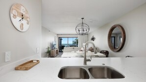 Una cocina moderna con encimera de mármol blanco, un lavabo doble y un reloj de pared de madera.