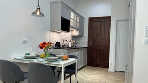 A modern kitchen with white cabinets, a wooden door, and a dining area with a table set for two. - Vintage Charm in Old Town Krakow -8 min walk to Krakow’s Main Square! Sleeps 6 (Kraków)