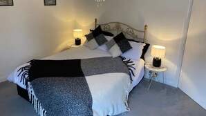 Un lit bien fait, recouvert d’une couverture à carreaux noirs et blancs, avec deux lampes de chevet et un lustre.