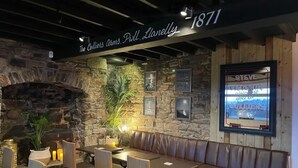 L’intérieur d’un restaurant avec un mur en pierre, un plafond en bois et une longue banquette servant de coin salon.
