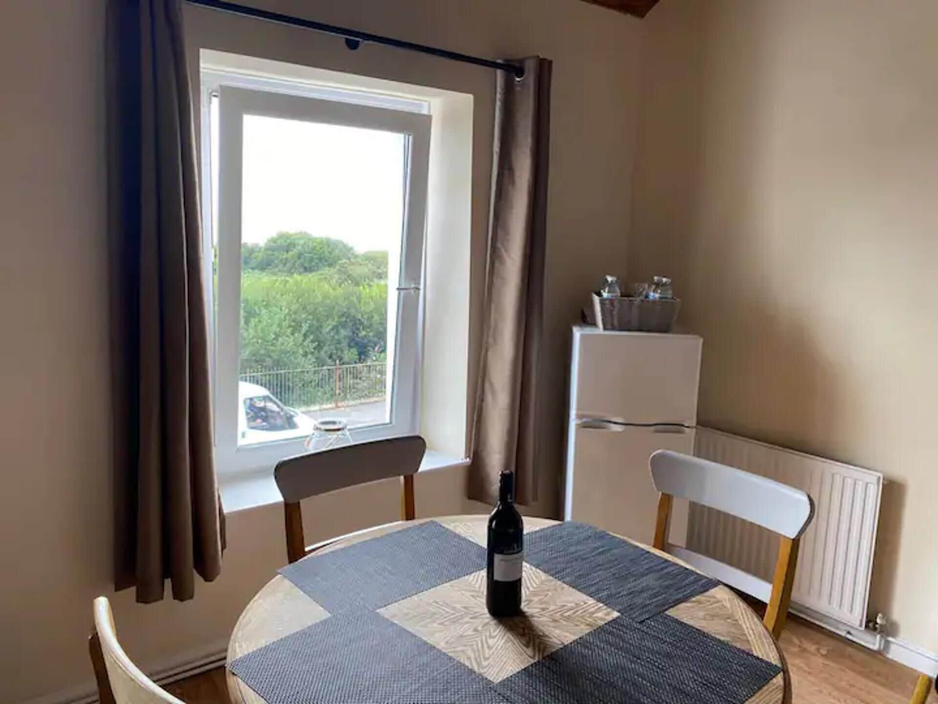 A small room with a round table, a bottle of wine, a chair, a radiator, and a window with curtains.