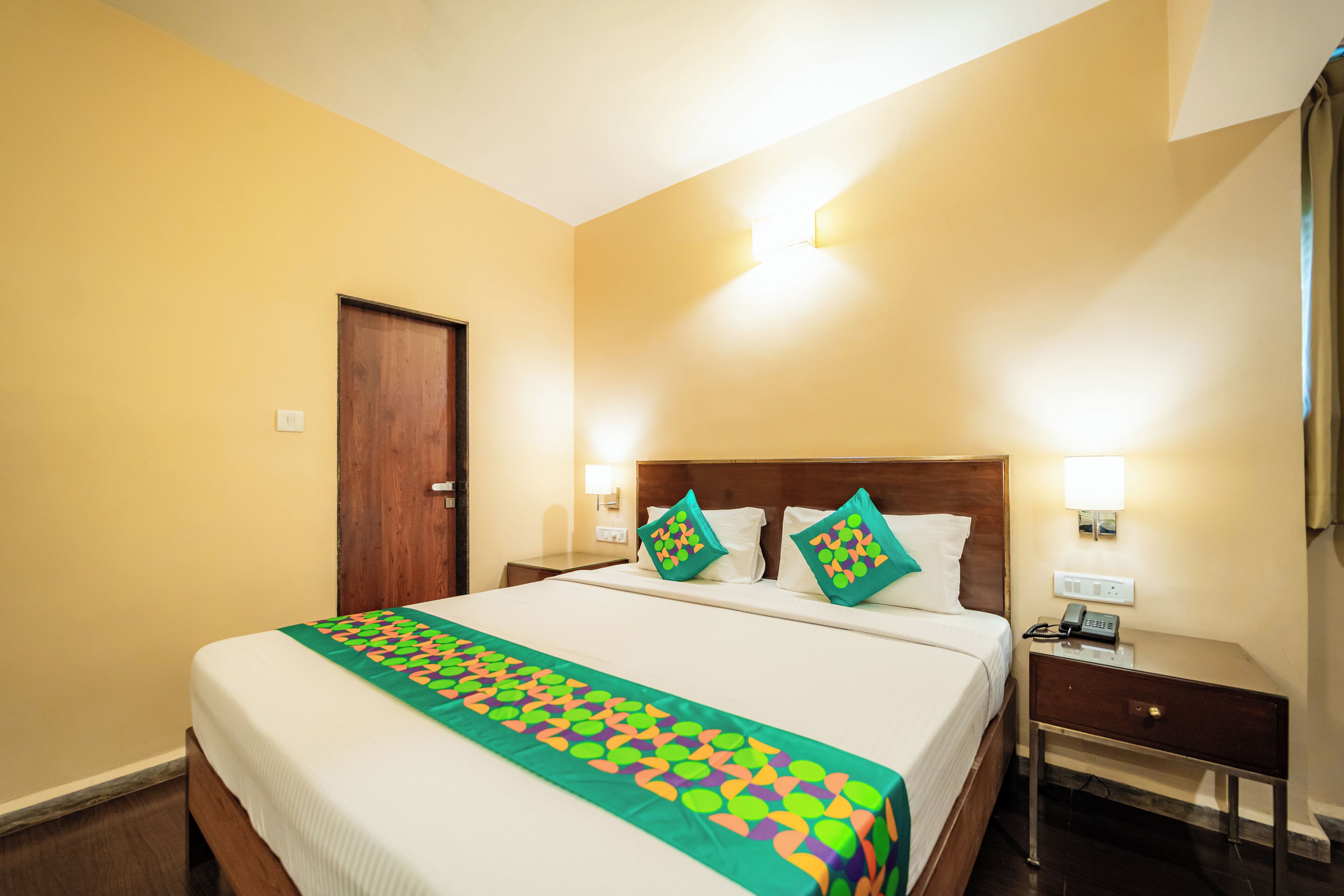 A hotel room with a large bed, two bedside tables, a nightstand, and a door.