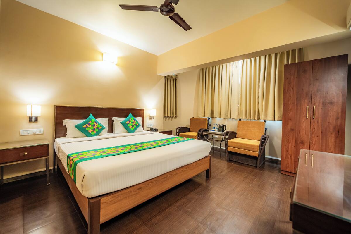 A hotel room with a large bed, a desk, a chair, a wardrobe, and a ceiling fan.