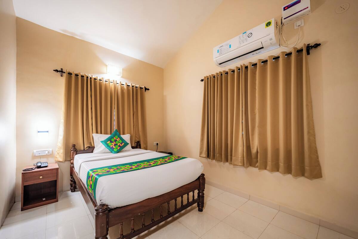 A hotel room with a wooden bed, beige walls, and an air conditioning unit.