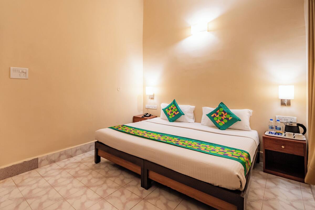 A hotel room with a bed, nightstands, a lamp, and a power outlet on the wall.