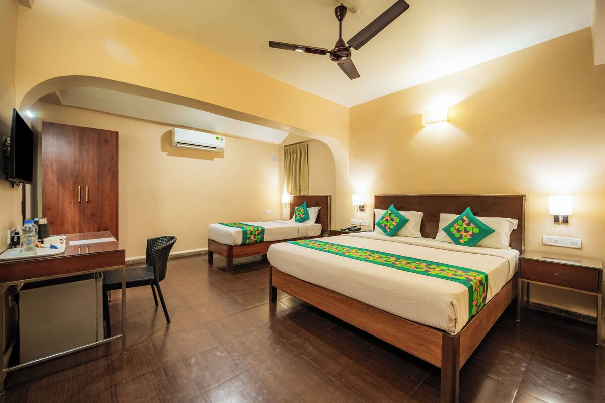 A hotel room with two single beds, a desk with a chair, a TV, and a ceiling fan.