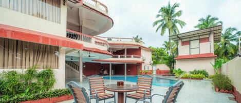 A hotel with a pool, outdoor seating, and a two-story building with balconies.