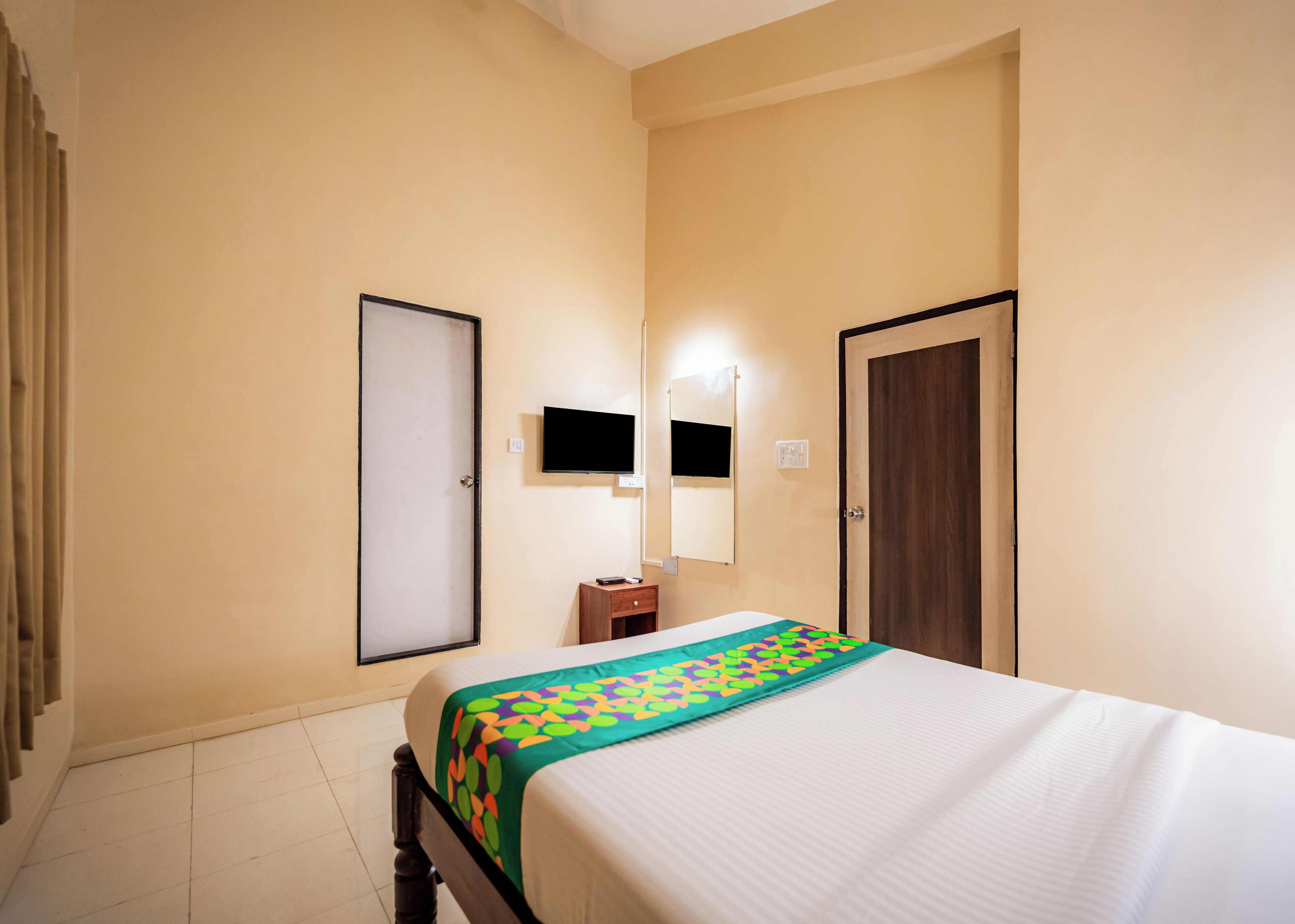 A hotel room with a bed, a bedside table, a TV mounted on the wall, and a door.