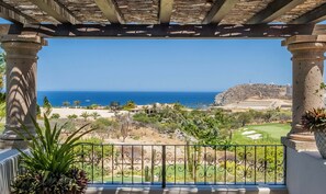 A view from a balcony with a pergola, overlooking a coastal landscape with a golf course, cacti, and a lighthouse. - Stunning Ocean Views, Private Pool, & Seaside Golf (Cabo San Lucas)