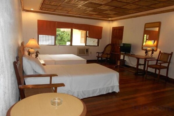A hotel room with two beds, a round table, a chair, and a desk with a lamp. - Sea Wind Resort (Boracay Island)
