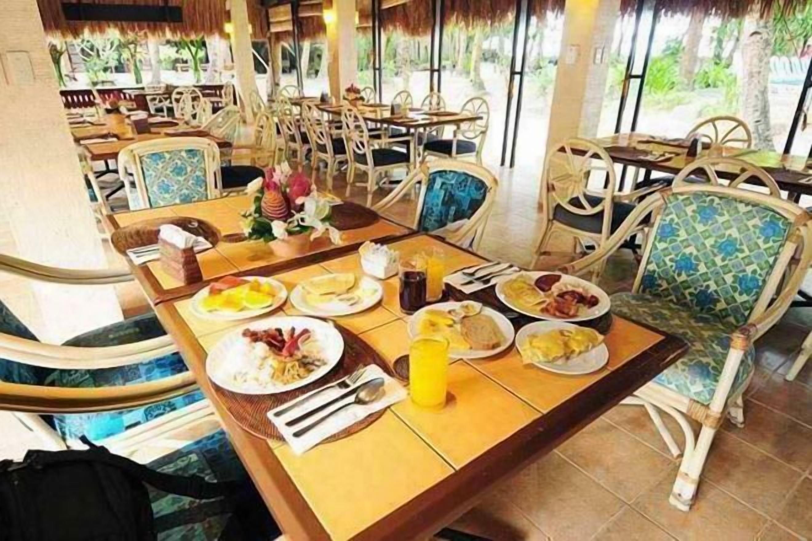 A dining area with tables and chairs, a pool, and a tropical view.
