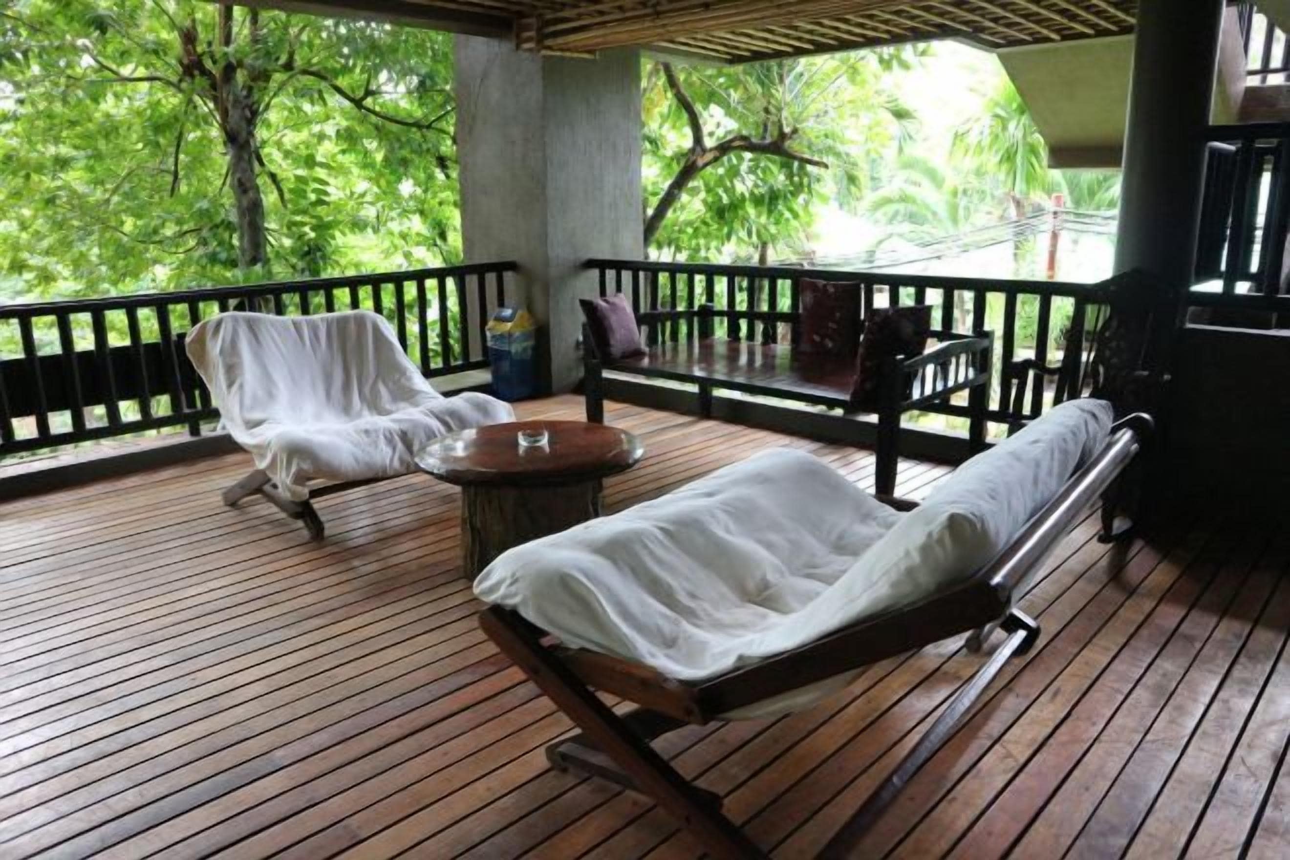 Une terrasse en bois avec deux chaises longues et une petite table, le tout entouré d’une rambarde noire.