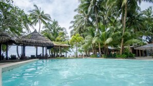 A swimming pool surrounded by palm trees and thatched-roof structures. - Sea Wind Resort (Boracay Island)
