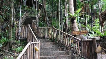 A wooden staircase with a sign that reads 'PLEASE WATCH YOUR STEP' in a forested area.