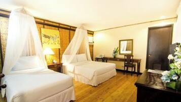 A hotel room with two beds, a desk, a chair, a nightstand, a lamp, a mirror, and a decorative plant.