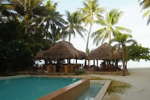 A pool area with thatched umbrellas, palm trees, and a beach setting. - Sea Wind Resort (Boracay Island)