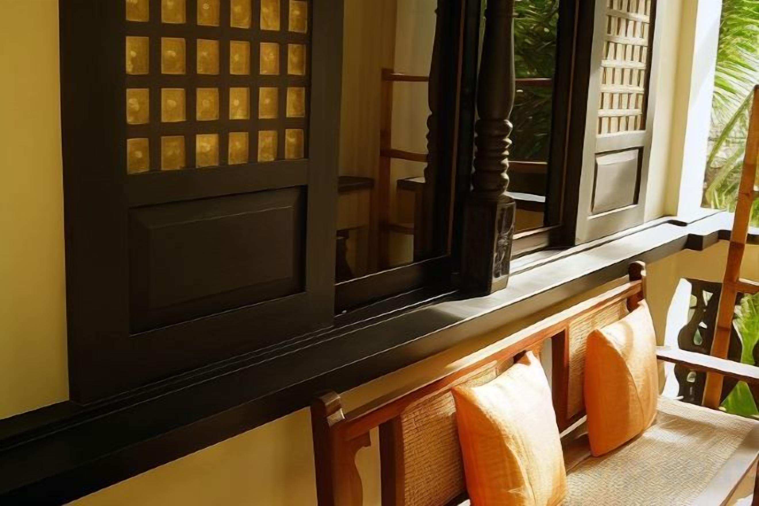 A window with a grid pattern, a wooden chair with a cushion, and a view of greenery outside.