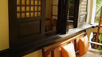 A window with a grid pattern, a wooden chair with a cushion, and a view of greenery outside.