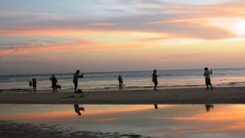 A beach scene with people walking and playing, and a calm sea reflecting the sky.