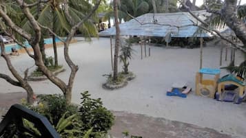 A sandy beach area with a shaded structure and a small playhouse.