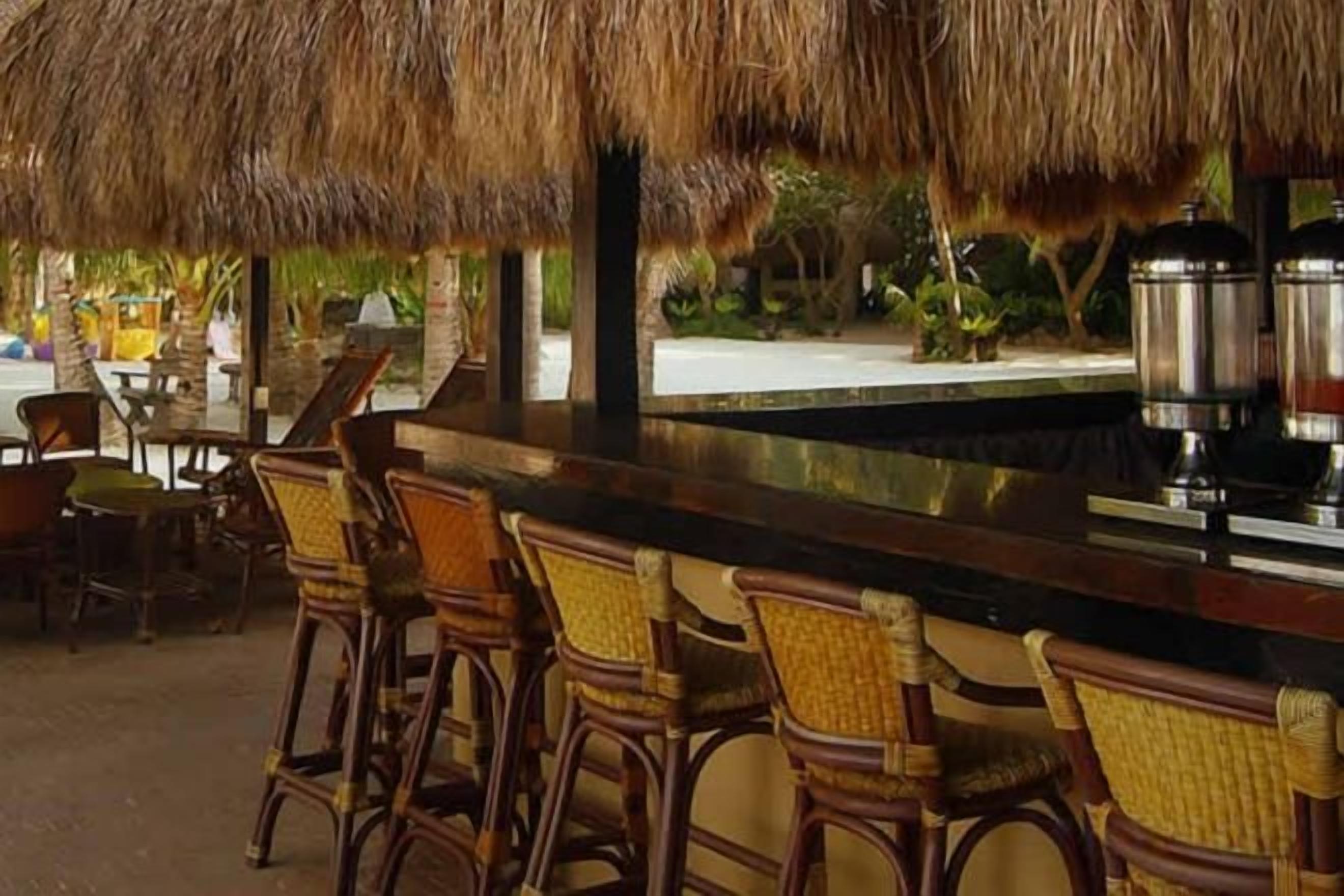 A bar area with wicker chairs and a thatched roof.