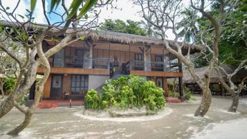 A two-story building with a thatched roof, surrounded by trees and a small garden.