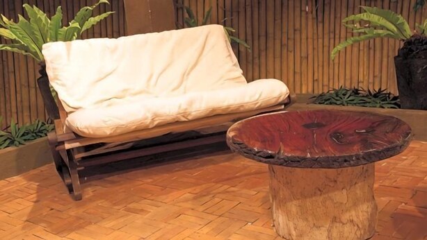 A wooden bench with a cushion, a round wooden table, and a bamboo fence in the background. - Sea Wind Resort (Boracay Island)