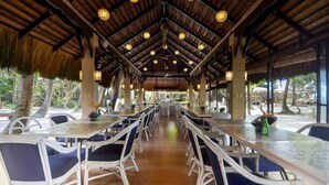 A covered dining area with tables and chairs, a thatched roof, and hanging light fixtures. - Sea Wind Resort (Boracay Island)