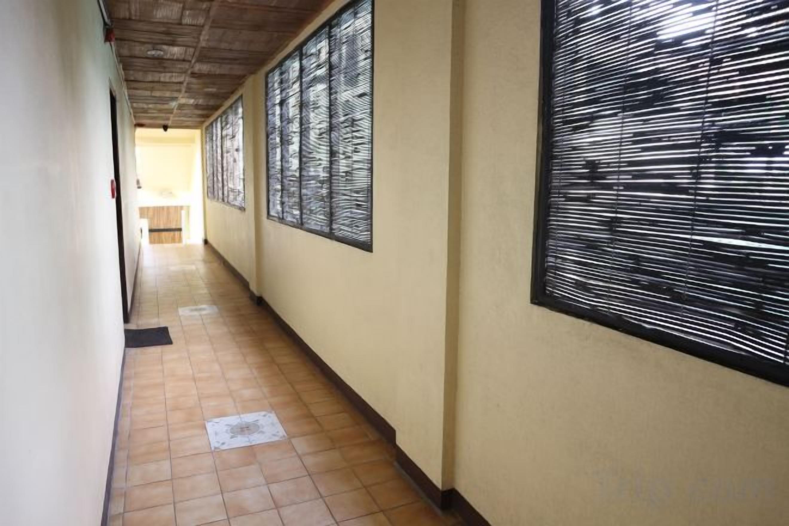 A corridor with tiled flooring, a ceiling with a wooden panel design, and a large window with a black frame.