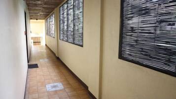 A corridor with tiled flooring, a ceiling with a wooden panel design, and a large window with a black frame.