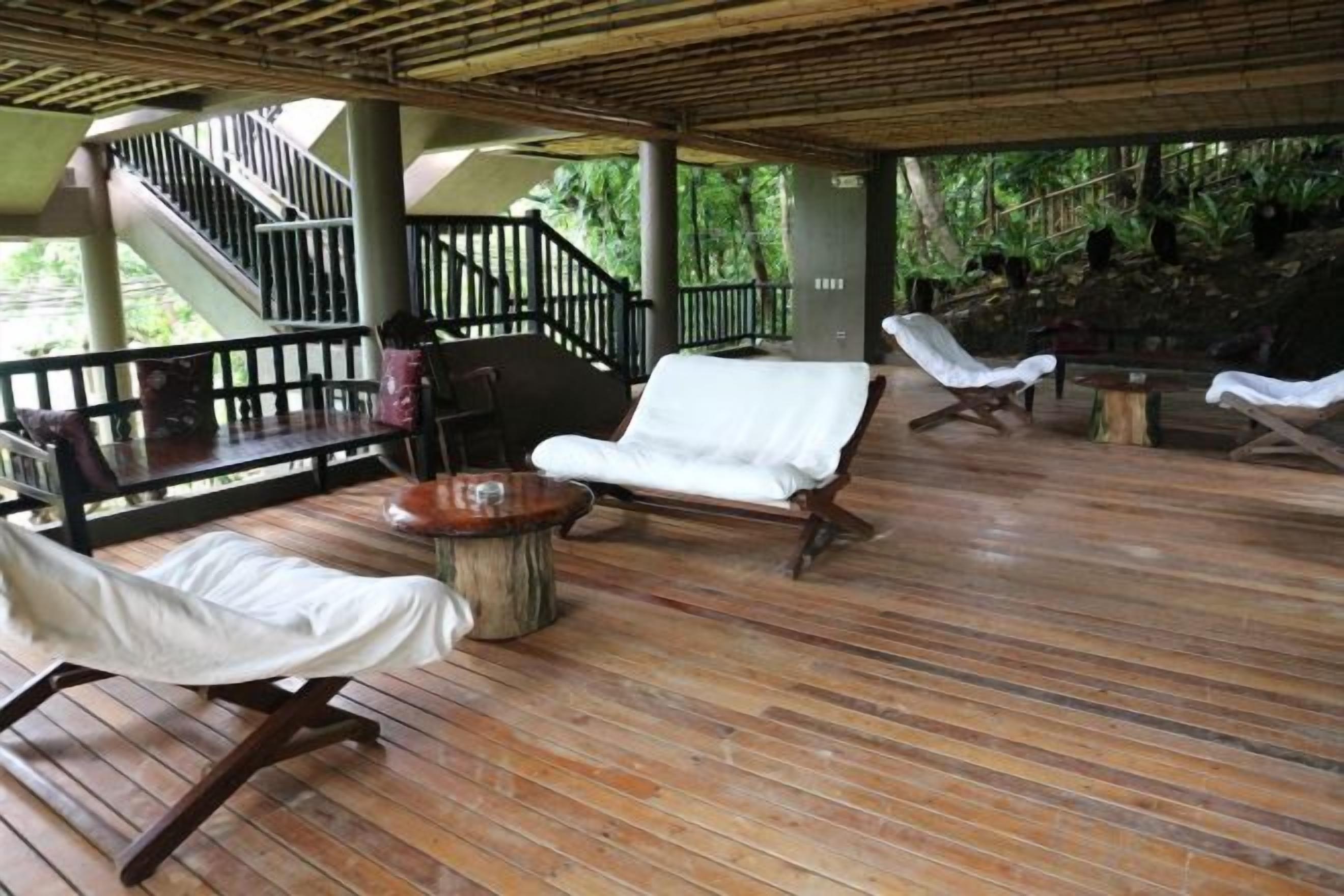 Un espacio al aire libre techado con suelo de madera, sillones de descanso y una escalera.