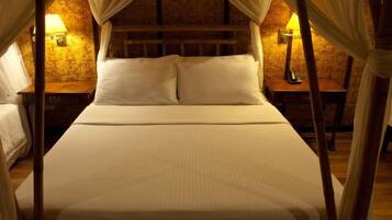 Una cama con dosel de cuatro postes, ropa de cama blanca, una pared de ladrillo y dos lámparas de noche.