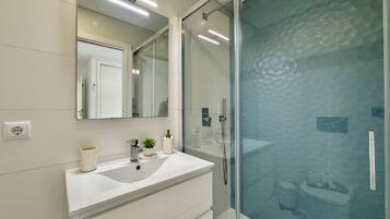 A modern bathroom with a glass shower enclosure, a white vanity with a mirror, and a sink.