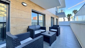 A modern outdoor patio with wicker furniture, large windows, and a view of the cityscape. - FARO PRESTIGE by HOMING (Faro)