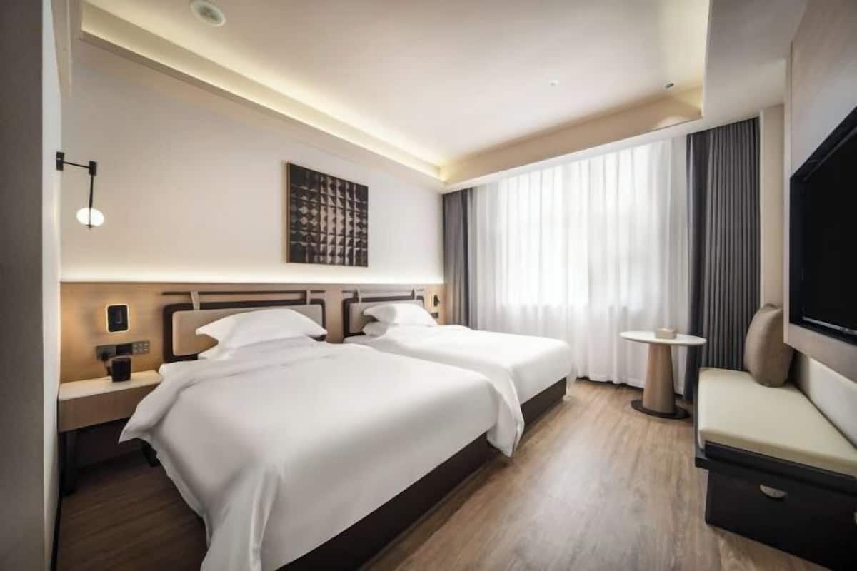 Ein Hotelzimmer mit zwei Betten, einem kleinen Tisch, einem Fernseher und einem großen Fenster mit Vorhängen.